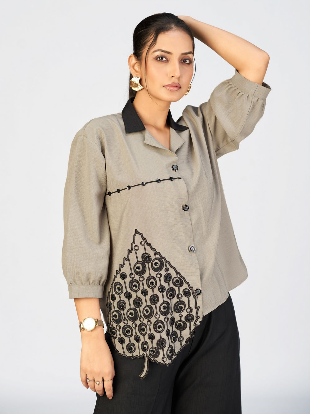 Woman wearing a beige embroidered shirt-style top with a bold black leaf appliqué design.