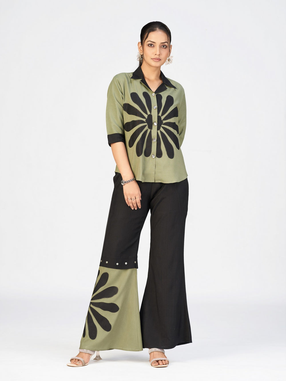 Woman wearing an olive green and black printed co-ord set with flared pants on a white studio background.