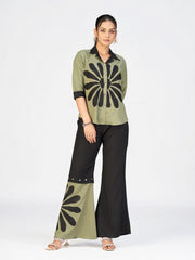 Woman wearing an olive green and black printed co-ord set with flared pants on a white studio background.