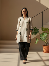 Woman wearing a beige embroidered kurti with black straight pants walking indoors.