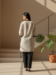 Full-length view of a model in a minimalist beige kurti featuring small embroidered motifs.