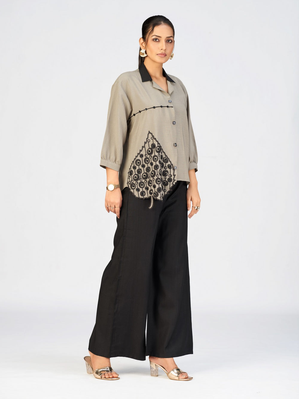 Model posing in a beige casual top with artistic embroidery and relaxed sleeves.