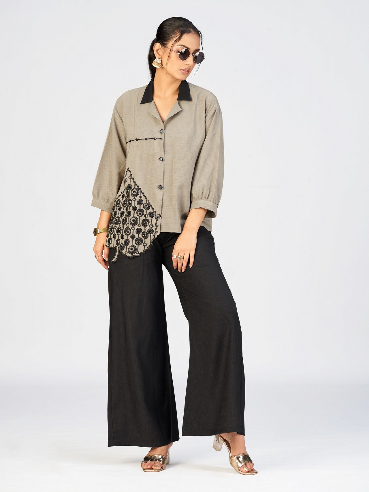 Fashion model wearing a beige button-up top paired with black pants in a studio setting.