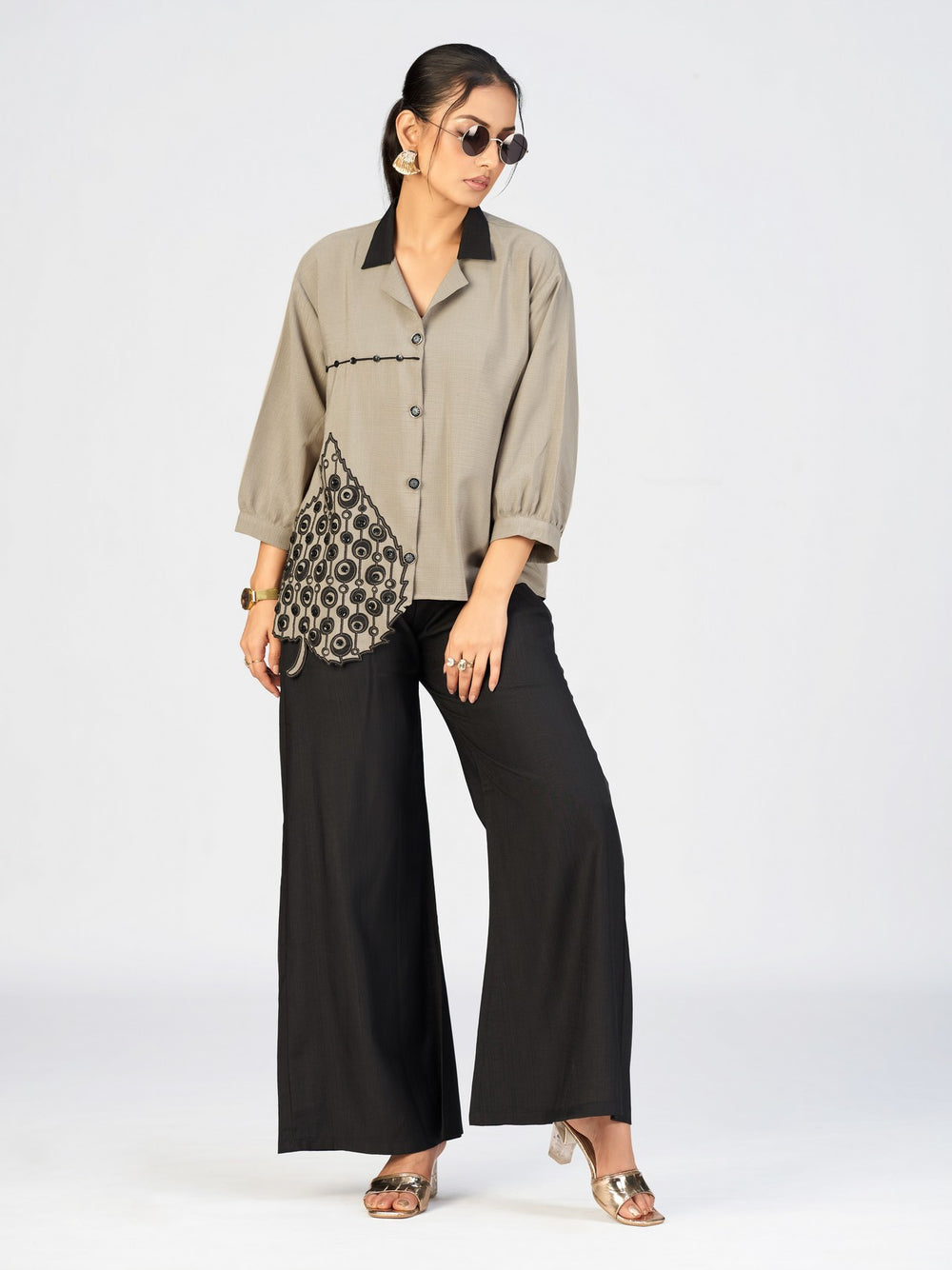 Fashion model wearing a beige button-up top paired with black pants in a studio setting.