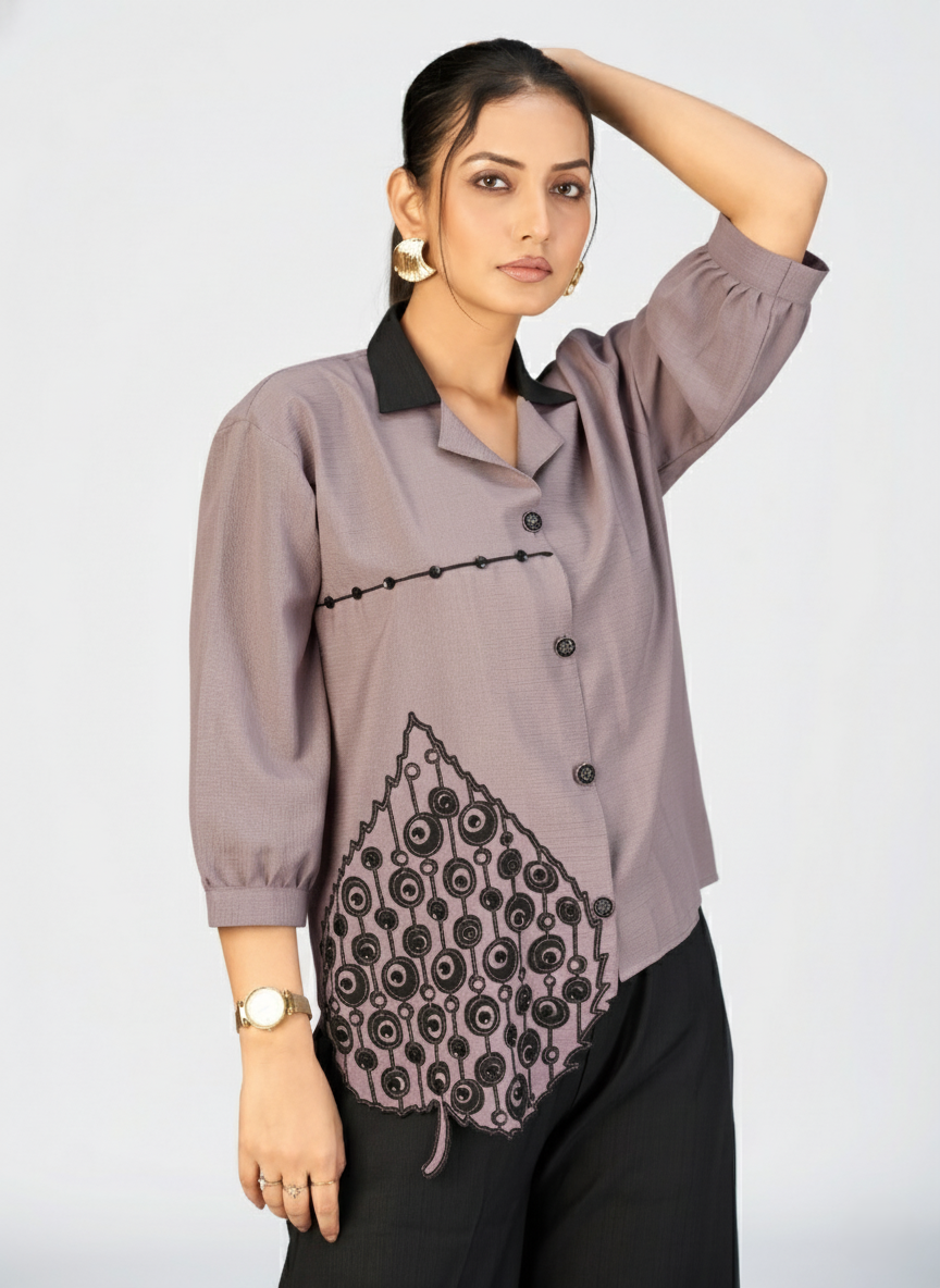 Studio shot of a woman modeling a beige top with unique leaf-shaped applique embroidery.