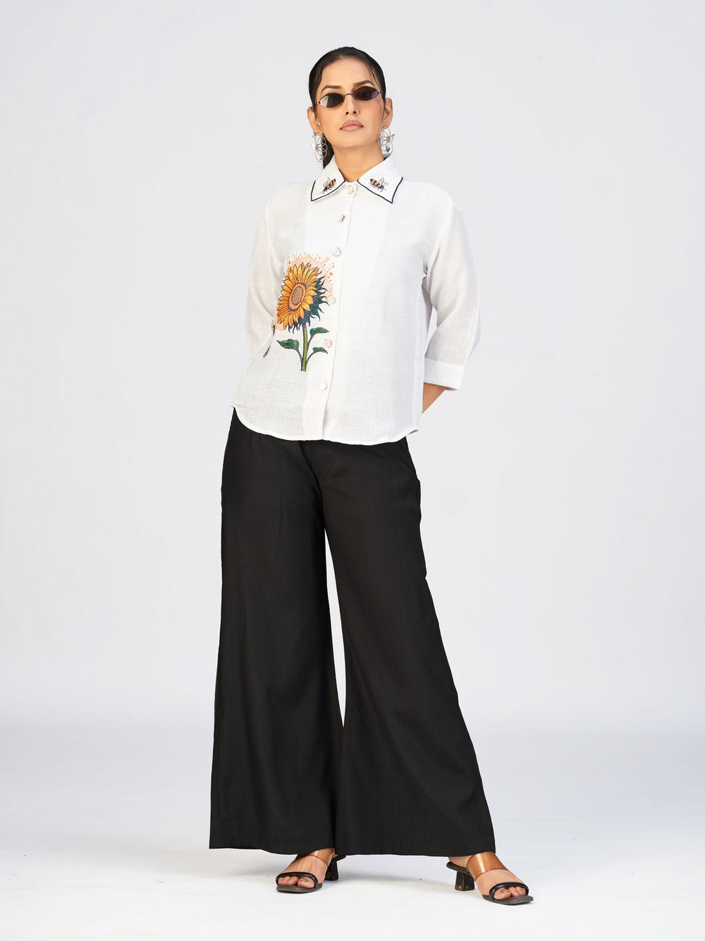 Woman wearing a white sunflower embroidered shirt top paired with black wide-leg pants.