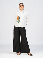Woman wearing a white sunflower embroidered shirt top paired with black wide-leg pants.