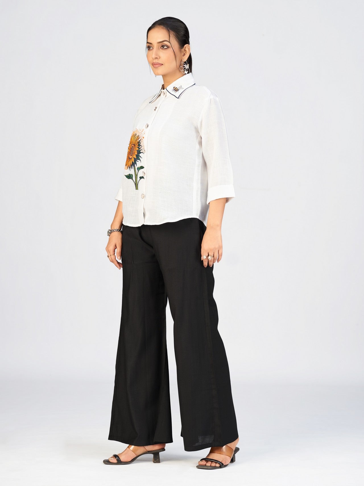 Model posing confidently in a white embroidered top and black flared pants.