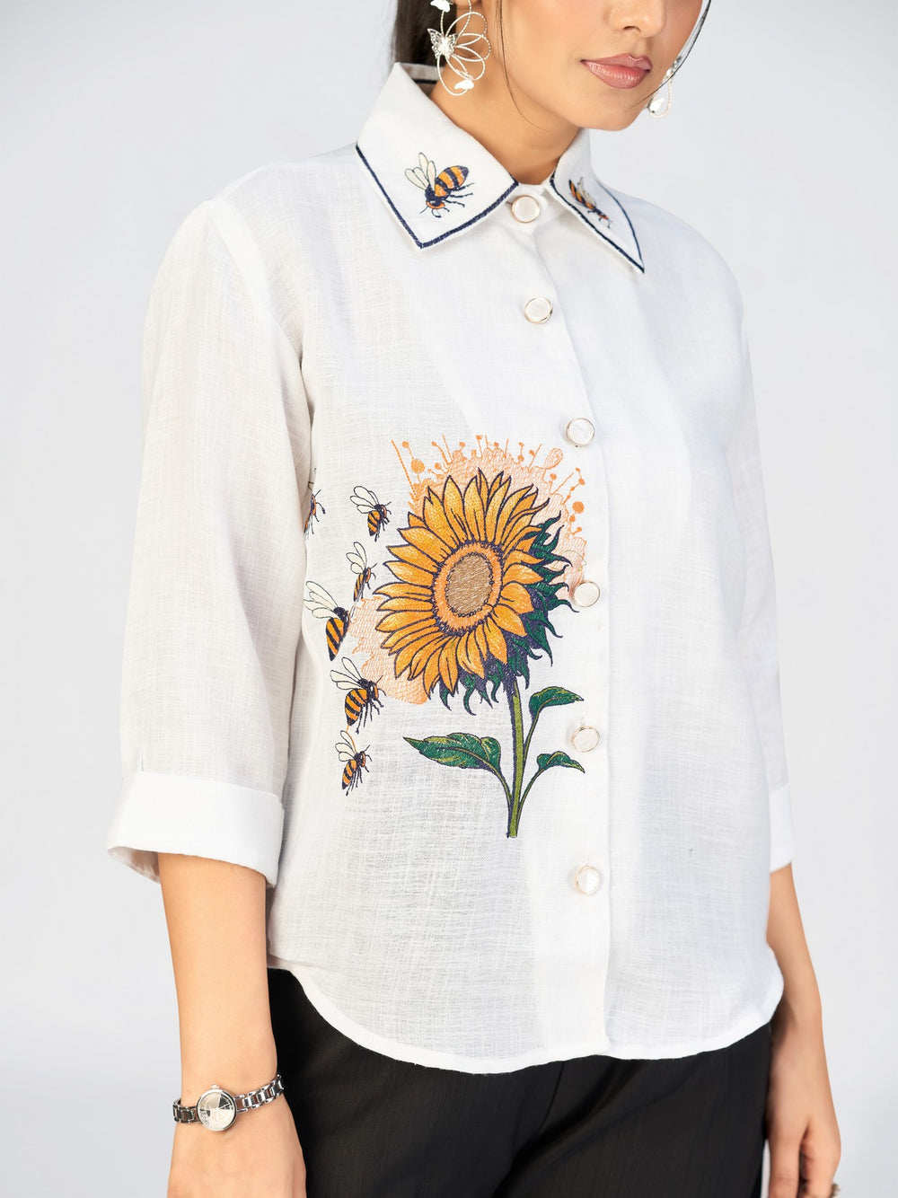 Full-length image of a woman in a white floral shirt top and wide-leg black trousers.