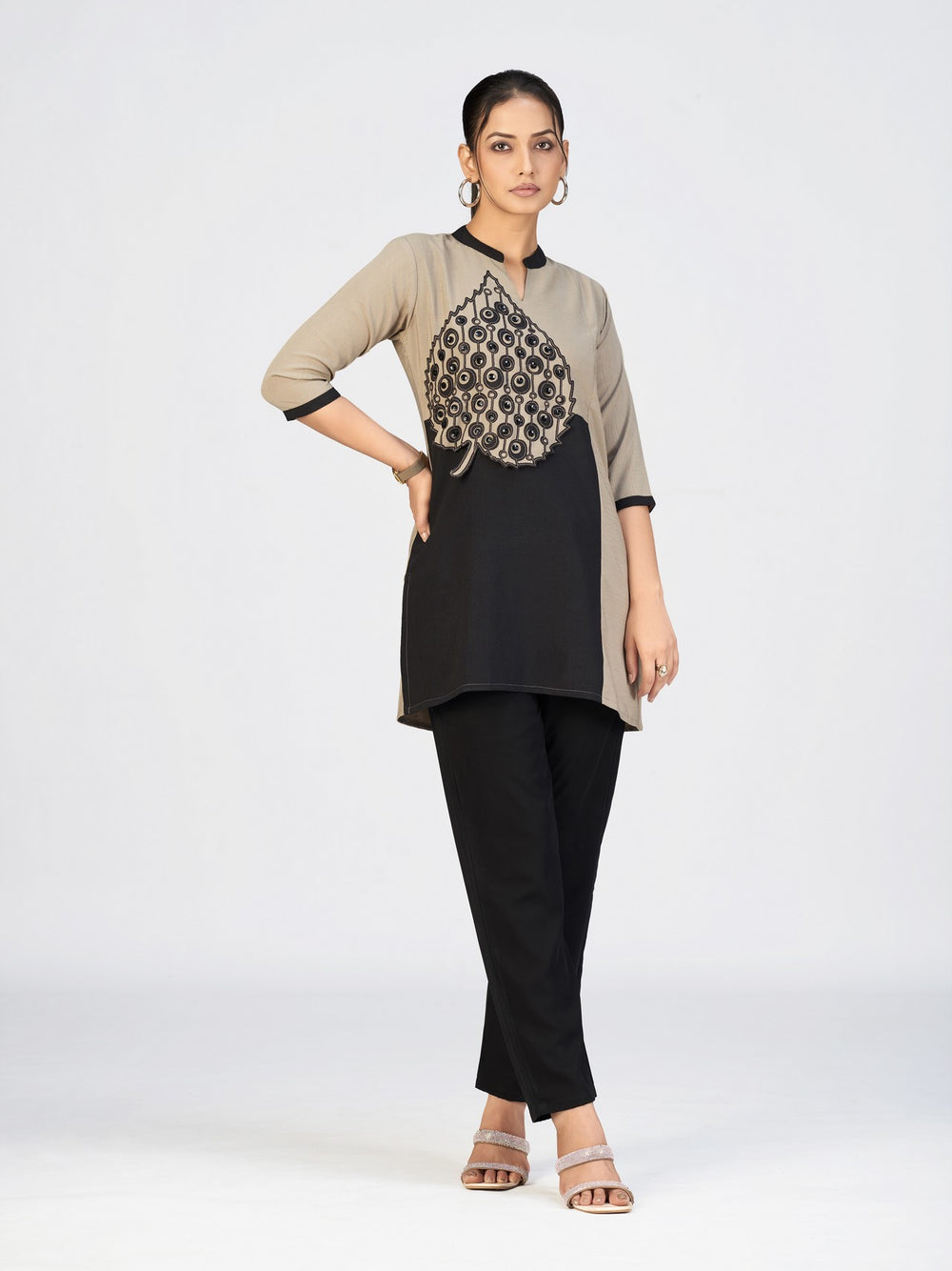 Woman wearing a dual-tone beige and black kurti with a bold embroidered leaf appliqué in front.