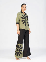 Elegant women’s two-piece outfit with a printed green shirt and black flared pants displayed by a model.