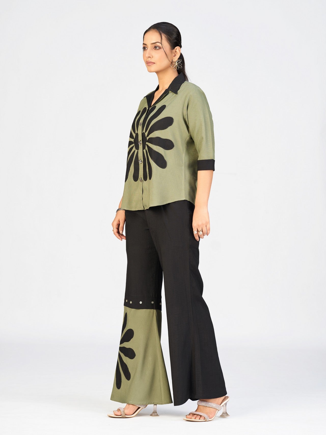 Full-length image of a woman dressed in a contemporary olive green co-ord set with decorative black detailing.